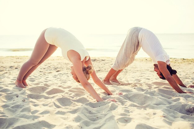 conceito de fitness, esporte, amizade e estilo de vida - casal fazendo exercícios de ioga na praia