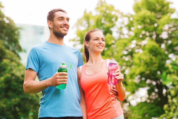 conceito de fitness, esporte, amizade e estilo de vida - casal sorridente com garrafas de água ao ar livre