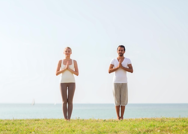 conceito de fitness, esporte, amizade e estilo de vida - casal sorridente fazendo exercícios de ioga ao ar livre