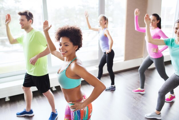 conceito de fitness, esporte, dança e estilo de vida - grupo de pessoas sorridentes com treinador dançando zumba no ginásio ou estúdio