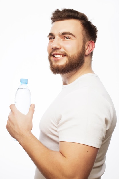 Conceito de fitness, esporte e estilo de vida: sorridente homem musculoso e esportivo, vestindo uma camisa branca com uma garrafa de água. Isolado no branco.