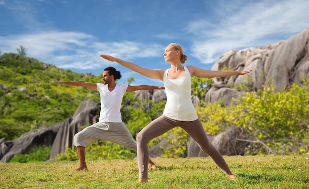 conceito de fitness, esporte e relaxamento - casal fazendo ioga em pose de guerreiro sobre fundo natural
