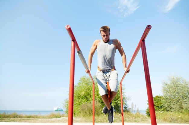 conceito de fitness, esporte, exercício, treinamento e estilo de vida - jovem fazendo mergulho de tríceps com cinto de peso em barras paralelas ao ar livre