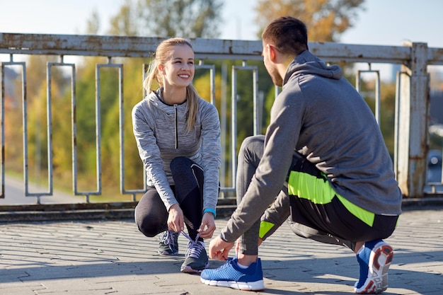 conceito de fitness, esporte, pessoas e estilo de vida - casal sorridente amarrando cadarços ao ar livre