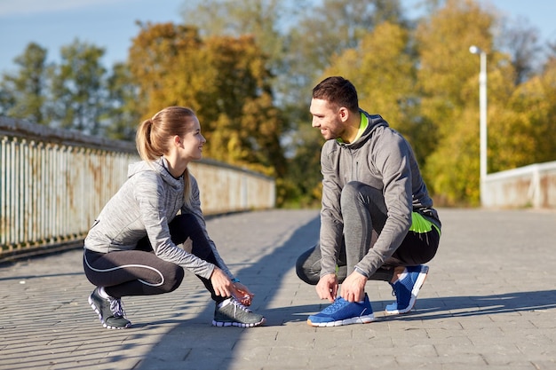 conceito de fitness, esporte, pessoas e estilo de vida - casal sorridente amarrando cadarços ao ar livre