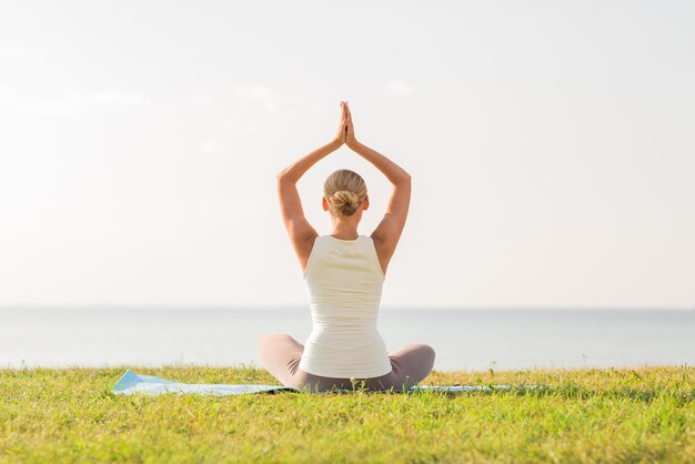 conceito de fitness, esporte, pessoas e estilo de vida - de mulher fazendo exercícios de ioga no tapete ao ar livre de trás