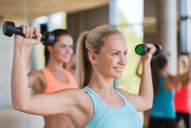 Conceito de fitness, esporte, pessoas e estilo de vida - grupo de mulheres se exercitando com halteres no ginásio