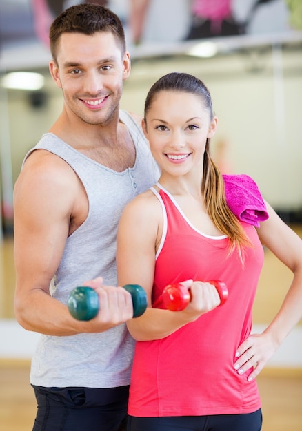 conceito de fitness, esporte, treinamento, academia e estilo de vida - duas pessoas sorridentes malhando com halteres na academia