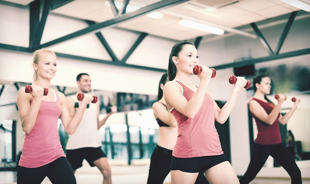 conceito de fitness, esporte, treinamento, academia e estilo de vida - grupo de pessoas sorridentes fazendo exercícios com halteres na academia