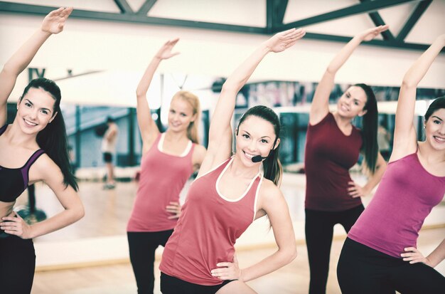 conceito de fitness, esporte, treinamento, academia e estilo de vida - grupo de pessoas sorridentes se alongando na academia