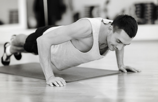 conceito de fitness, esporte, treinamento, academia e estilo de vida - homem sorridente fazendo flexões na academia