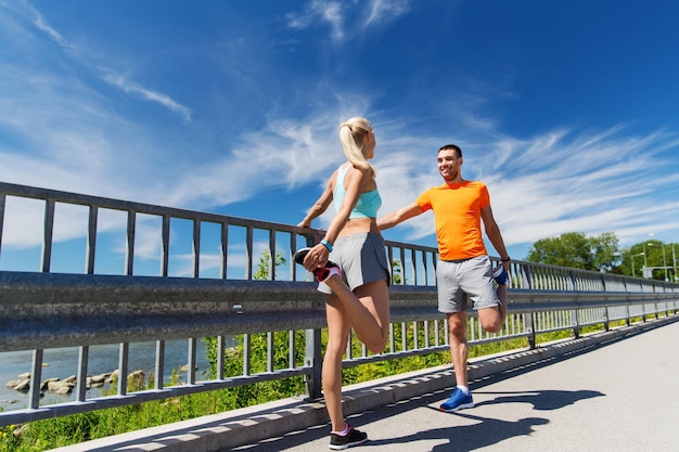 conceito de fitness, esporte, treinamento e estilo de vida - casal sorridente esticando ao ar livre