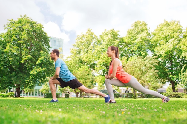 Conceito de fitness, esporte, treinamento e estilo de vida - casal sorridente esticando ao ar livre