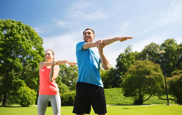 conceito de fitness, esporte, treinamento e estilo de vida - casal sorridente esticando ao ar livre