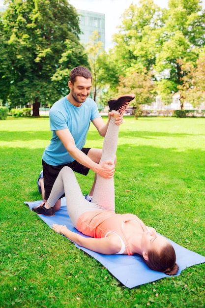 Conceito de fitness, esporte, treinamento e estilo de vida - casal sorridente se estendendo no tapete ao ar livre