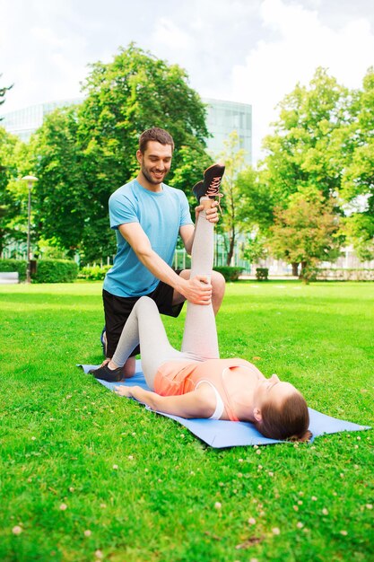 conceito de fitness, esporte, treinamento e estilo de vida - casal sorridente se estendendo no tapete ao ar livre