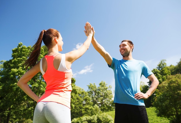 conceito de fitness, esporte, treinamento e estilo de vida - duas pessoas sorridentes fazendo mais cinco ao ar livre