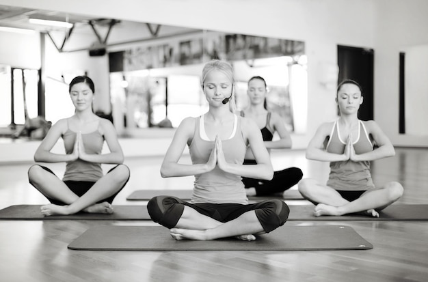 conceito de fitness, esporte, treinamento, ginástica e estilo de vida - grupo de mulheres sorridentes com o treinador meditando em pose de ioga