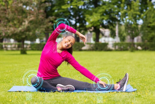 conceito de fitness, esporte, treinamento, parque e estilo de vida - mulher sorridente esticando a perna no tapete ao ar livre