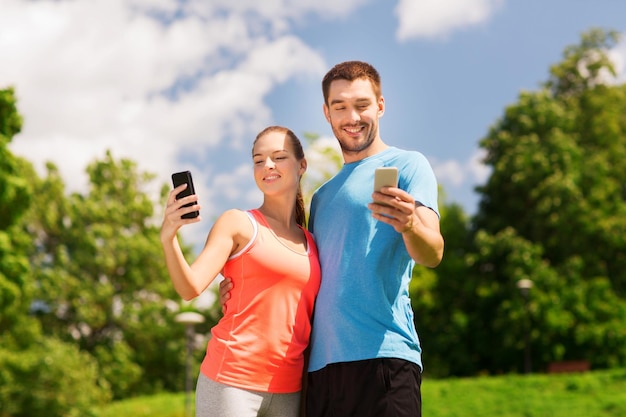 conceito de fitness, esporte, treinamento, tecnologia e estilo de vida - duas pessoas sorridentes com smartphones ao ar livre