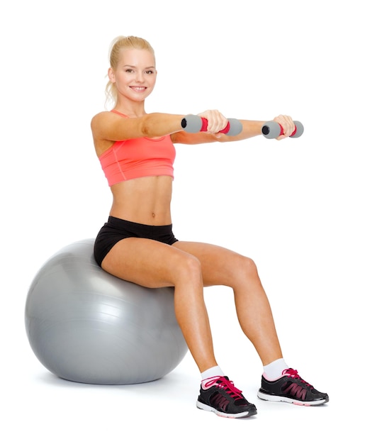conceito de fitness, exercício e dieta - mulher desportiva sorridente com halteres sentado na bola de fitness