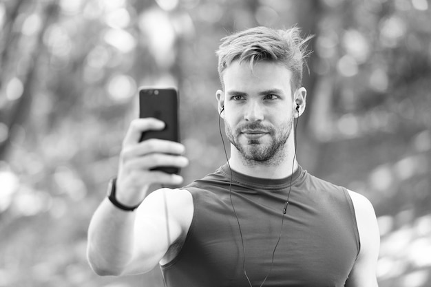 Conceito de gadget de esporte Telefone móvel de atleta configurar lista de reprodução antes de correr Cara de atleta de homem ocupado configurando fundo de natureza de aplicativo de smartphone Treinamento de esportista com pedômetro e fones de ouvido