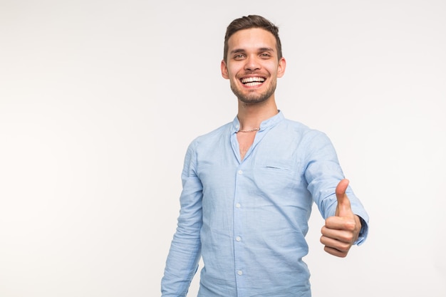 Conceito de gesto e pessoas - homem bonito com sorriso aparecendo o polegar sobre fundo branco, com espaço de cópia.