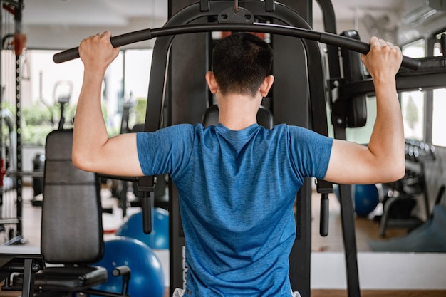 Conceito de ginásio de treinamento: um adolescente do sexo masculino usando um equipamento de ginástica puxando seus braços musculosos