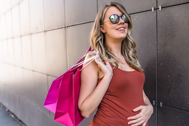Conceito de gravidez, maternidade, pessoas e expectativa - grávida sorridente feliz com sacolas de compras na rua da cidade