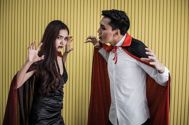 Conceito de Halloween de uma jovem mulher asiática na fantasia de bruxa e o homem asiático na fantasia de Drácula em fundo amarelo. Casal adolescente do retrato vestido de bruxas e Drácula para celebrar o festival de Halloween.