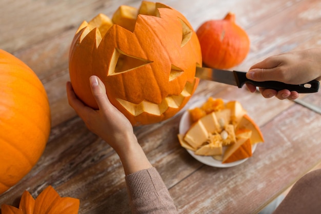 conceito de halloween, decoração e feriados - close de mulher com faca esculpindo abóbora ou lanterna em casa