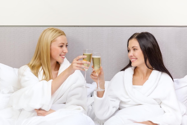 conceito de hotel, viagem, amizade e felicidade - amigas sorridentes com taças de champanhe na cama