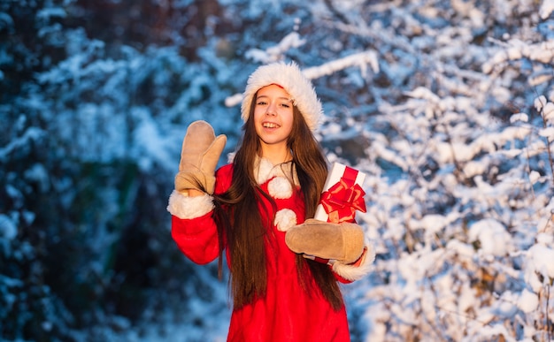 Conceito de infância feliz. Felicidade e alegria. Chapéu de Papai Noel de criança. Presentes do Papai Noel. Manhã gelada de Natal. Hora de milagres. Pai Natal generoso. Criança feliz garota ao ar livre natureza nevada. Feliz Natal.