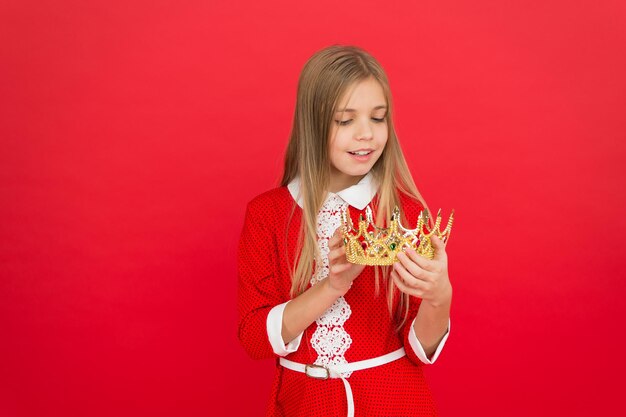 Conceito de infância feliz Toda garota sonhando se tornar princesa Lady princesinha Garota sorriso bonito segure a coroa enquanto está fundo vermelho Melhor prêmio para mim Criança segura o símbolo da coroa dourada da princesa