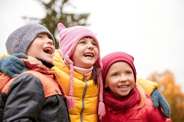 conceito de infância, lazer, amizade e pessoas - grupo de crianças felizes abraçando e rindo no parque outono
