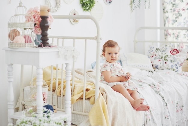 Conceito de infância. menina vestido bonito localização na cama brincando com brinquedos em casa. Childroom vintage branco