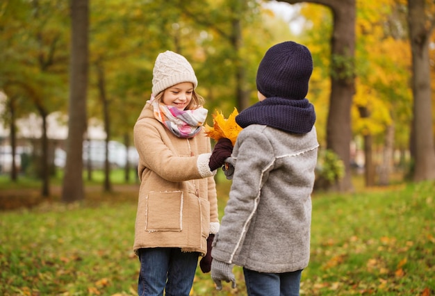 conceito de infância, temporada e pessoas - sorridente menina e menino com folhas de outono no parque