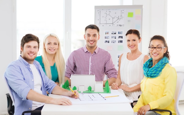 conceito de inicialização, educação, arquitetura e escritório - arquitetos sorridentes com modelo de casa e planta trabalhando no escritório