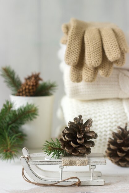 Conceito de inverno com blusa branca pulôver, luvas, trenós, copo, cones e ramos de abeto.