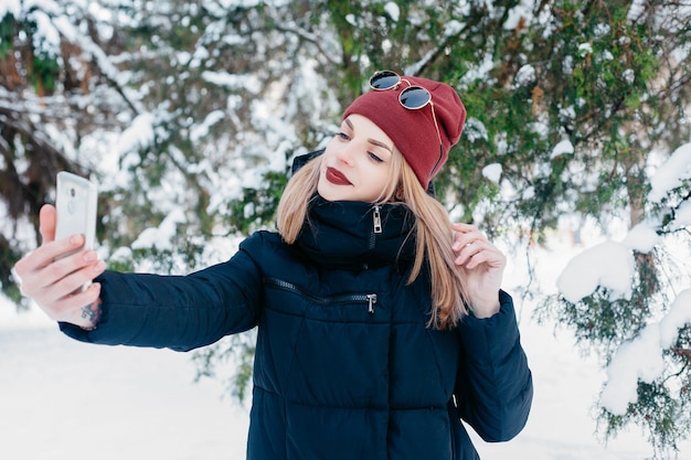 Conceito de inverno, Natal, tecnologias, pessoas, estilo de vida e beleza - TEMPO DE SELFI. Menina bonita morena, fazendo um selfie com seu telefone inteligente. Mulher jovem e bonita. Retrato de inverno ao ar livre.