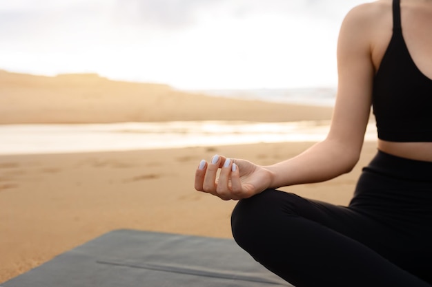 Conceito de ioga ao ar livre recortado de senhora irreconhecível meditando em roupas esportivas sentada na esteira de fitness