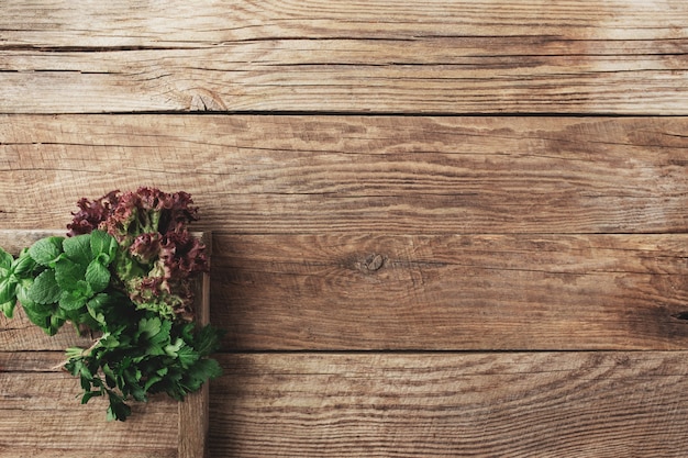 Conceito de jardinagem e alimentação saudável com diferentes ervas e folhas de salada em fundo de madeira em recipiente de madeira