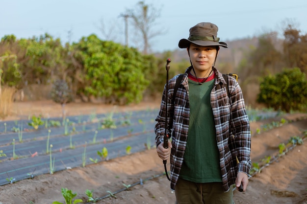 Conceito de jardinagem: um jovem agricultor pulverizando um pesticida químico para prevenir as plantações das pragas.