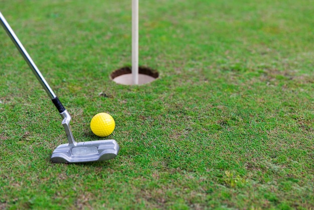 conceito de jogo, entretenimento, esporte e lazer - close-up do clube de metal e bola perto do buraco no campo de golfe verde