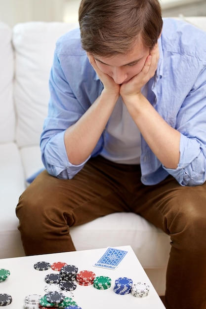 Foto conceito de jogo, jogo e falha - homem perdedor com cartas de baralho e fichas na mesa em casa