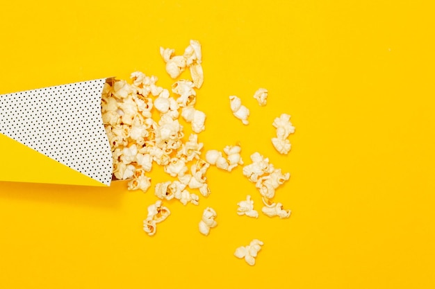 Conceito de lanche Pipoca doce derramada do copo de papel em fundo amarelo