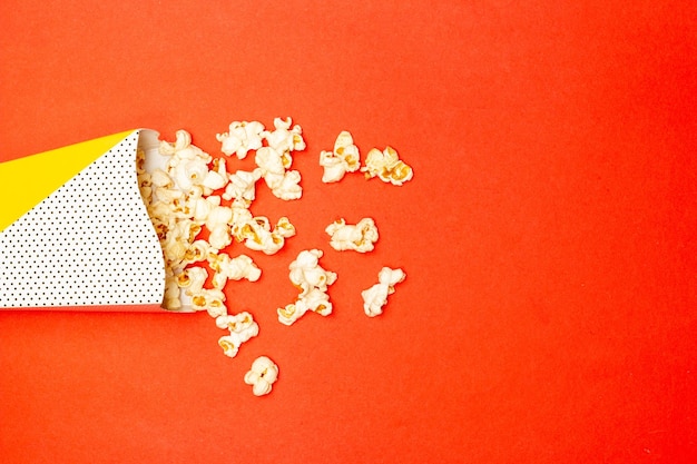 Foto conceito de lanche pipoca doce derramada do copo de papel em fundo vermelho