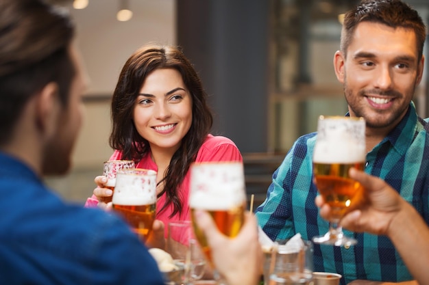 Conceito de lazer, alimentação, alimentos e bebidas, pessoas e feriados - amigos de sorriso jantando e bebendo cerveja no restaurante ou pub