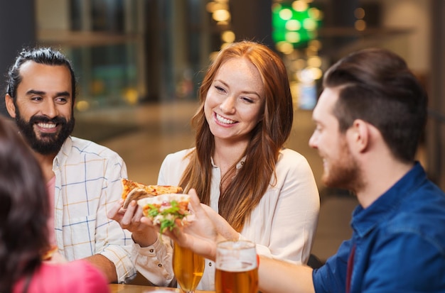 Foto conceito de lazer, comida e bebidas, pessoas e feriados - amigos sorridentes comendo pizza e bebendo cerveja no restaurante ou pub