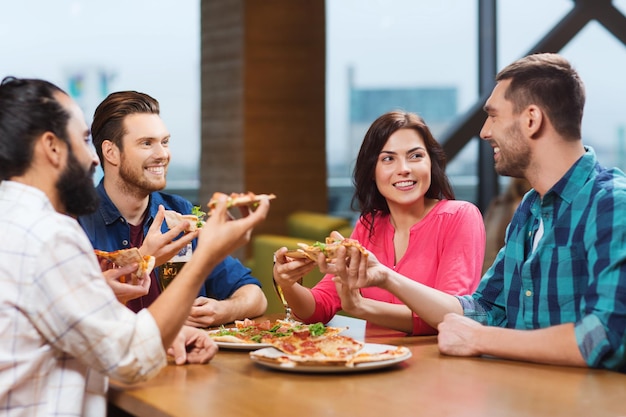 Foto conceito de lazer, comida e bebidas, pessoas e feriados - amigos sorridentes comendo pizza e bebendo cerveja no restaurante ou pub